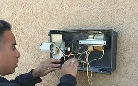 Electrician working on an open exterior electrical box on a stucco wall with the wiring pulled out